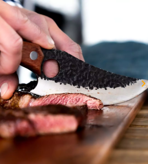 close up of man using Huusk Knife to cut meet